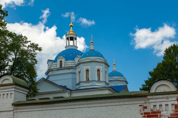 Fototapeta na wymiar White orthodox church with blue domes and golden crosses surrounded by a high stone fence