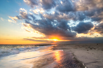 Sun burst breaking through soft colorful clouds as the sun sets over an empty open beach. Long Island New York