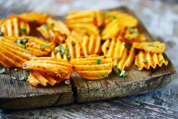 Selective focus. Wavy potato chips with spices on a wooden board. Unhealthy food. Fast food.