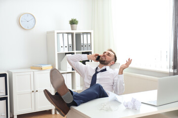 Lazy young man talking on smartphone in office