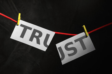 Cut word TRUST hanging on rope against black background. Concept of jealousy
