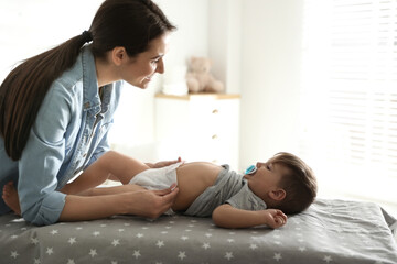 Mother changing baby's diaper on table at home