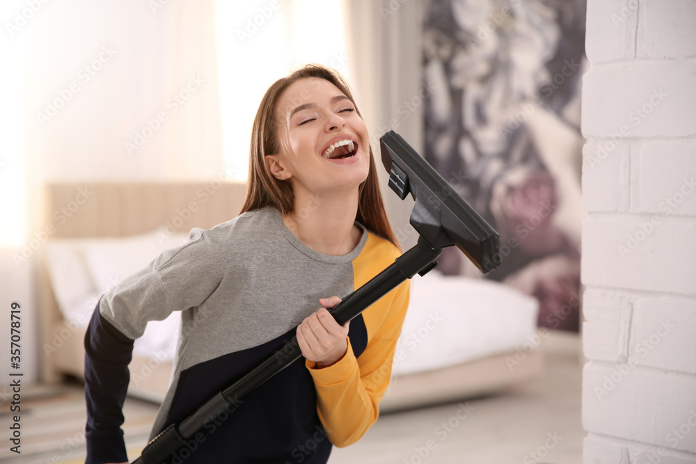 Wall mural Young woman having fun while vacuuming at home