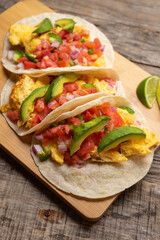 Breakfast egg tacos with flour tortilla and fresh sauce on wooden background