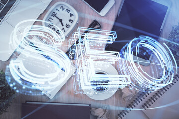 Double exposure of SEO hologram drawing over desktop. Top view. Search optimization concept.