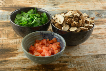 Ingredients of chopped spinach, mushrooms and tomatoes in ceramic bowls prepared for cooking