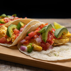 Breakfast egg tacos with flour tortilla and fresh sauce on wooden background