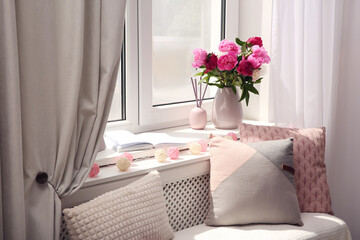 Comfortable place for rest with cushions and peony flowers near window indoors