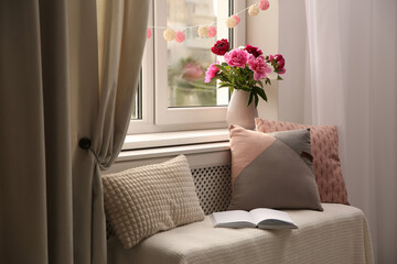 Comfortable place for rest with cushions and peony flowers near window indoors