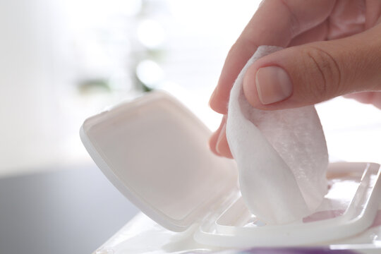 Woman taking wet wipe from pack on blurred background, closeup