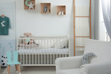 Stylish baby room interior with crib and armchair