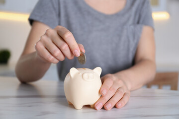 Obraz na płótnie Canvas Woman putting money into piggy bank at marble table indoors, closeup