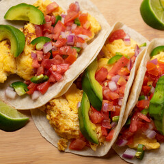 Breakfast egg tacos with flour tortilla and fresh sauce on wooden background
