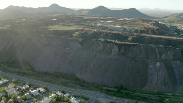 Aerial shot of houses in town by open-pit mine on sunny day, drone flying forward over residential structures - Bisbee, Arizona