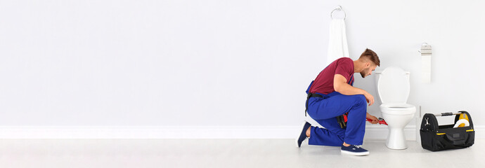 Young man working with toilet bowl in bathroom, space for text. Banner design