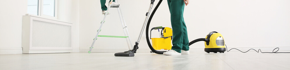 Professional young janitor using vacuum cleaner indoors, closeup view. Banner design