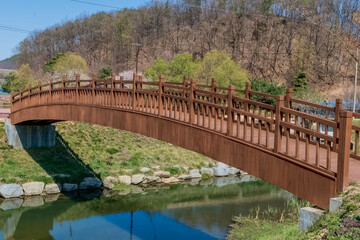 Side view of wooden footbridge over small stream in rural public park.