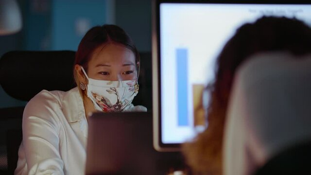 Young Female Asian Professional Rhythmically Moving Head Side to Side in Protective Face Mask While Working Late in Office