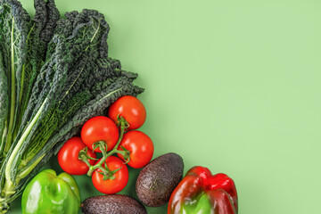 Vegetable creative layout on green background. Black kale leaves, tomatoes branch, red and green bell pepper, avocado. Vegetarian healthy food concept. Flat lay, copy space. Farmer produce