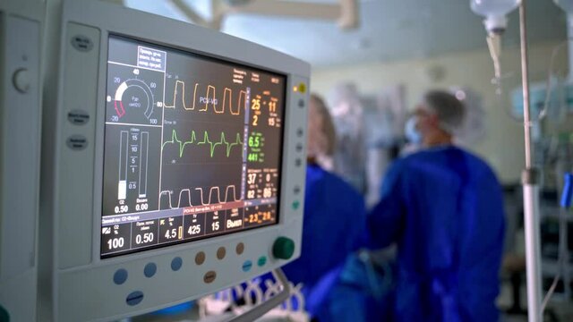 Hospital monitor in the operating room. Screen shows vital signs of a patient on the background of surgical procedure. Teamwork of doctors.