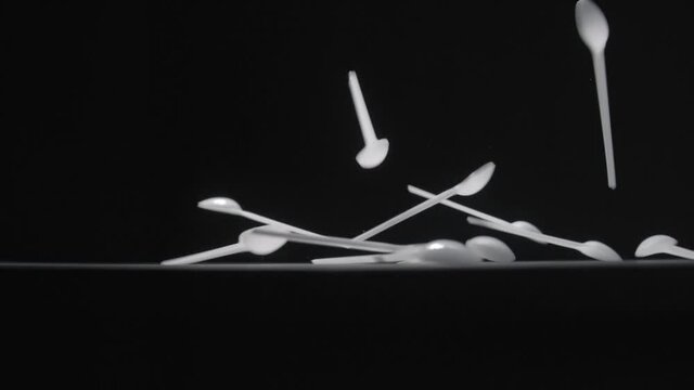 White teaspoons falls on black background slow motion video.