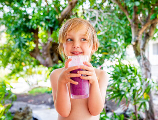 Healthy boy drinks delicious fruit smoothie outside during summer.