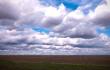 rural landscape with field, gray ground and beautiful cloudy sky