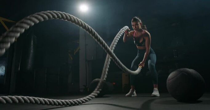 Active dedicated motivated female athlete training in gym with battle ropes, determined confident girl enjoying bodybuilding achieving goals with healthy lifestyle 4k footage