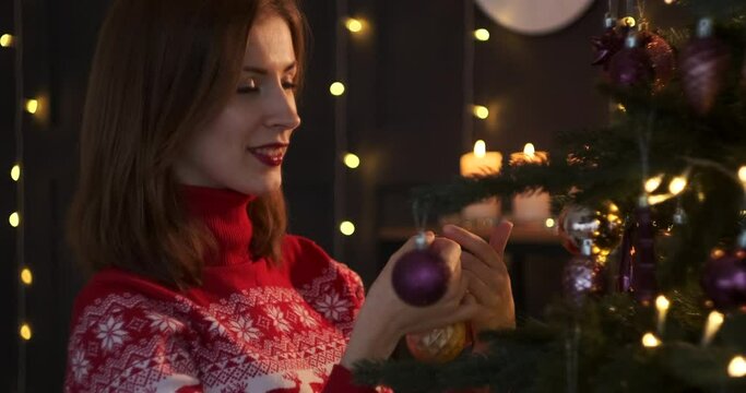 Beautiful woman in turtleneck sweater decorating Christmas tree