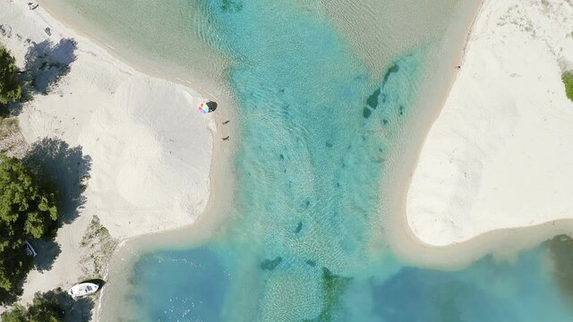 Directly above aerial footage of natural lagoon with unrecognizable swimming people. The Glarokavos lagoon on the east coast of Kassandra, Halkidiki, Greece