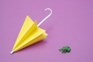 紫色のバックに折り紙の黄色い傘とカエルのフィギア