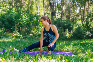 Naklejka na ściany i meble Young woman doing yoga exercises in summer city park.