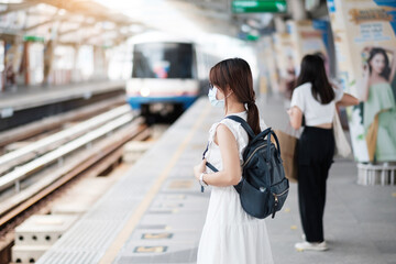 young Asian woman wearing Surgical face mask protect coronavirus inflection at public train station. social distancing, new normal and life after covid-19 