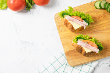 Delicious croissant sandwich with fresh Ham, cheese,  tomato, cucumber and lettuce on white background. Top view with copy space. Flat lay.
