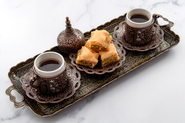 Ramadan treat, Eid Mubarak and arabian hospitality concept with picture of turkish baklava and mini coffee cups on authentic mediterranean metal tray isolated on white marble background