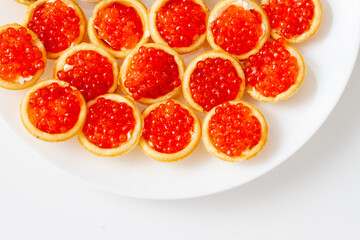 Fototapeta na wymiar Tartlets with red caviar on white plate. Red caviar top view