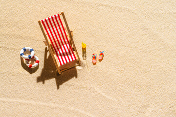 Fototapeta na wymiar Aerial view of one deck chair, sunbed, lounge, glass of orange juice, flip flops, Lifebuoy on sandy beach. Summer and travel concept. Minimalism