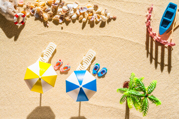 Aerial view of a sandy beach with two  umbrellas, pair of flip flops, palm tree, boat, shells, sunbed. Summer and travel concept.