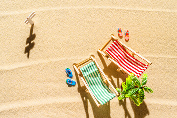 Aerial view of two deck chair, sunbed, lounge, flip flops, palm tree on sandy beach. Summer and travel concept. Minimalism