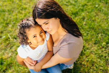 Lovely ecuadorian woman hugging, walking, caressing and caring her mixed race dark skinned daughter in summer vacation, outdoor at city street.