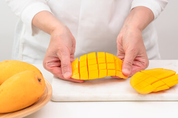 Fresh ripe organic yellow mangoes close up. Woman cutting mango on white cutting board, preparing...