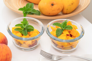 Chopped mangoes and peaches in a glass bowls with mint leaves close up on kitchen table. Fresh fruit salad, delicious dessert
