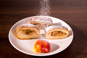 Strudel with apples, sliced ​​on a white plate with sprinkled sugar powder close-up
