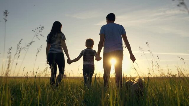 Happy family. Mom dad and son in an outdoor team walk through a green meadow at sunset. Healthy, active lifestyle of a married couple. Parents with a child have fun.