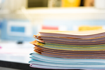 Stack of documents in multicolored paper files on desktop in office.