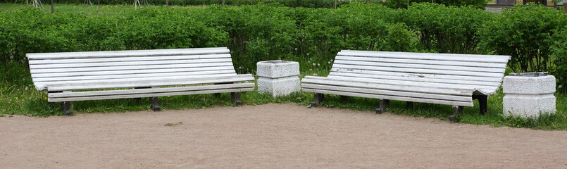 Two white wooden Park benches with a trash can between them
