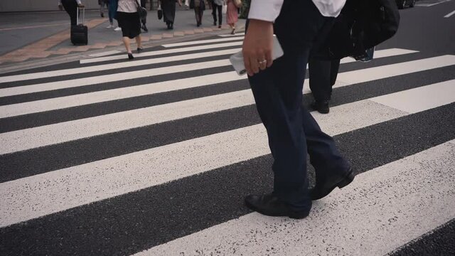 Business commuters walking across the street in the crosswalk from the waist down in slow motion