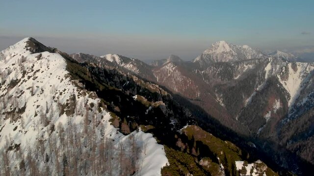 Drone camera panning from left to rigth showcasing the entire karavanke alps mountains range. Aerial view of the Karavanke Alps in the winter on a clear skies day.
