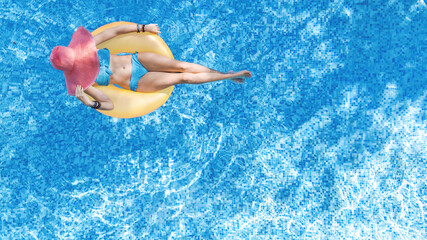 Beautiful woman in hat in swimming pool aerial top view from above, young girl in bikini relaxes and swims on inflatable ring donut and has fun in water on family vacation, tropical holiday resort
