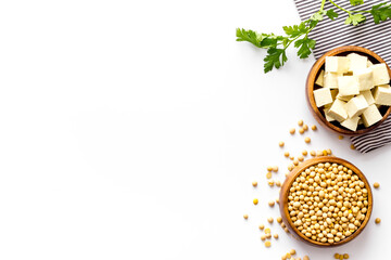Tofu cubes in bowl and soybeans on white background top-down space for text